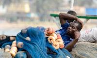 Ghanaian men rest on the fishing net in Elmina port. (123rf.com)