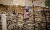 A woman stands near the fence of her house. © FAO/Luis Tato