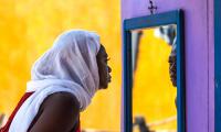 African Ghana woman standing in front of a mirror with a white shawl covering her hair. 123rf