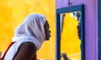 African Ghana woman standing in front of a mirror with a white shawl covering her hair. 123rf